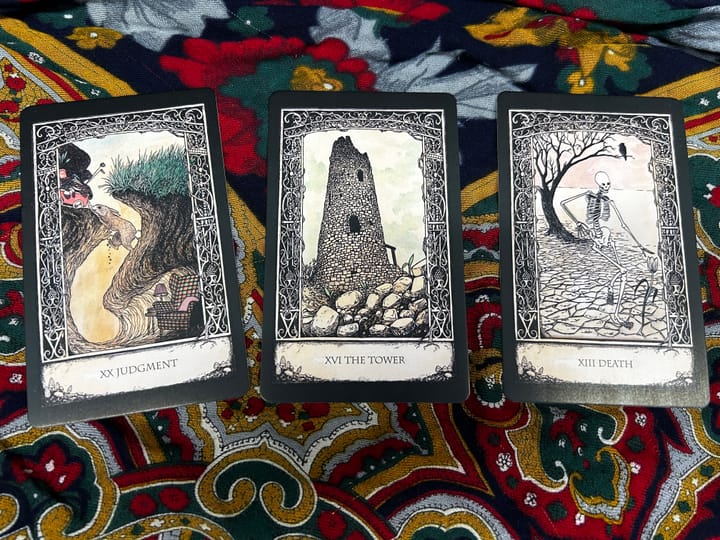 Three tarot cards from the "Tarot of Tales" by Melinda Lee Holm on a jewel-toned, folk-patterned scarf. The cards are Judgment, which shows a rabbit carrying things out of its burrow; Th